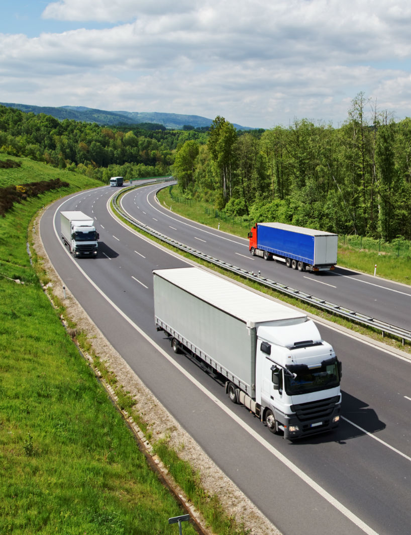 Trucks traveling on an asphalt highway between forests